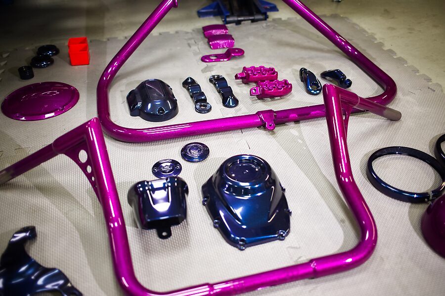 Rahmenbügel und Kleinteile einer Harley in Magenta, daneben Deckel in Chamäleon