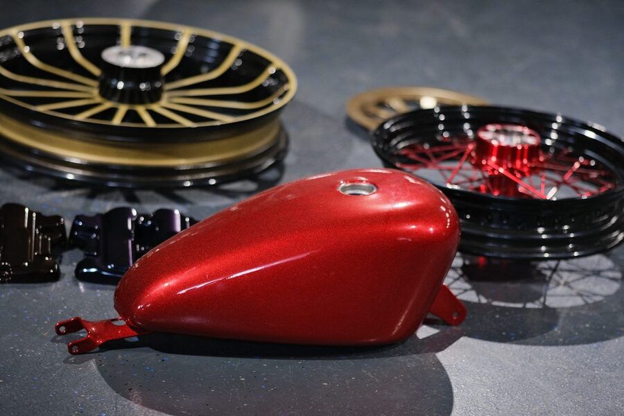 Motorradtank in Rot metallic beschichtet, im Hintergrund beschichtete Räder
