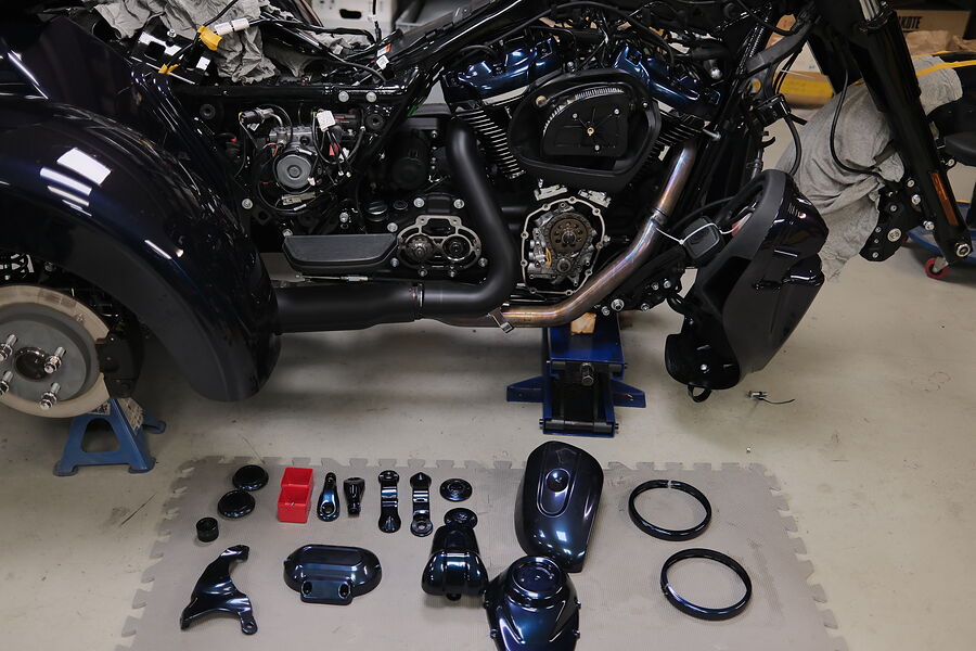 Beschichtete Anbauteile einer Harley in Chamäleon-Effektfarbe, aufgereiht vor der zerlegten Maschine