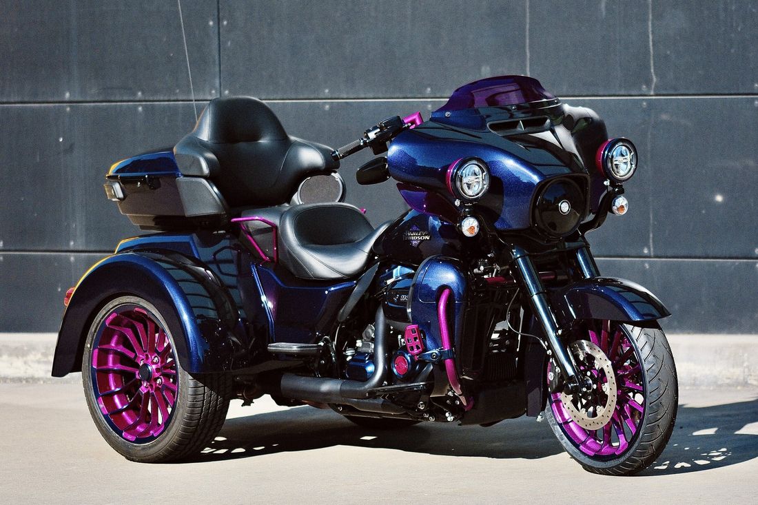 Harley-Davidson Trike in Blauviolett mit Felgen in Magenta, Seitenansicht vor einer dunklen Fassade